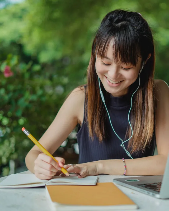 Cô gái đeo tai nghe ôn ngữ pháp, ghi chép bên laptop