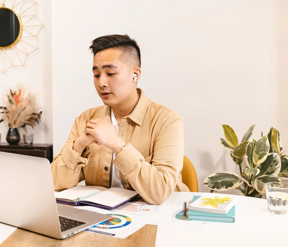 Chàng trai làm bài kiểm tra trên laptop, ghi chép vào sổ