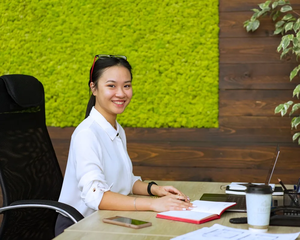 Cô gái mỉm cười bên bàn làm việc có sổ và bút