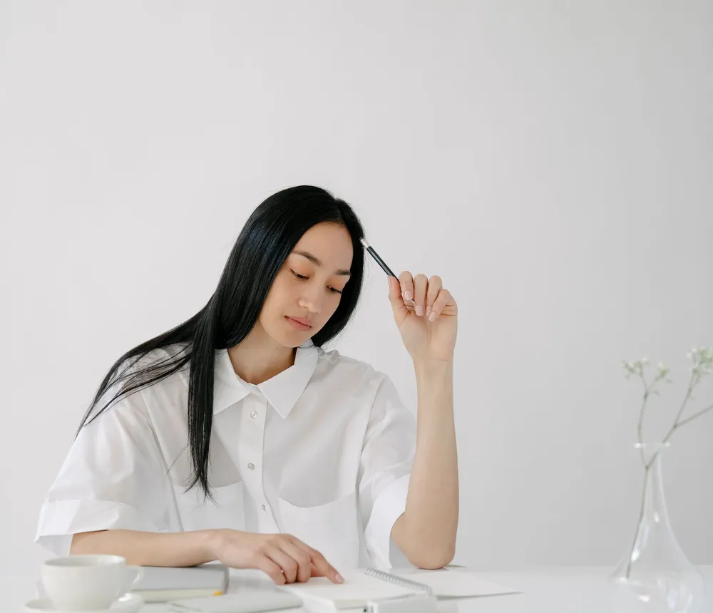 Cô gái cầm bút suy nghĩ bên cuốn sổ tay